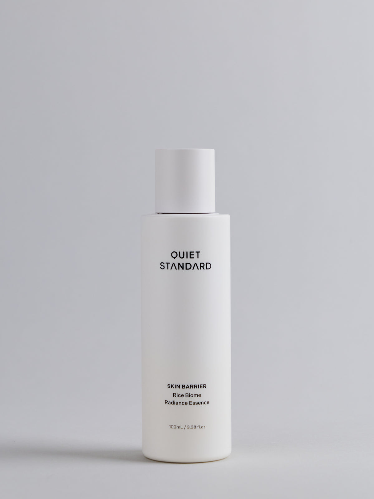 A white cylindrical bottle of Quiet Standard Skin Barrier Rice Biome Radiance Essence, centered against a light gray background.